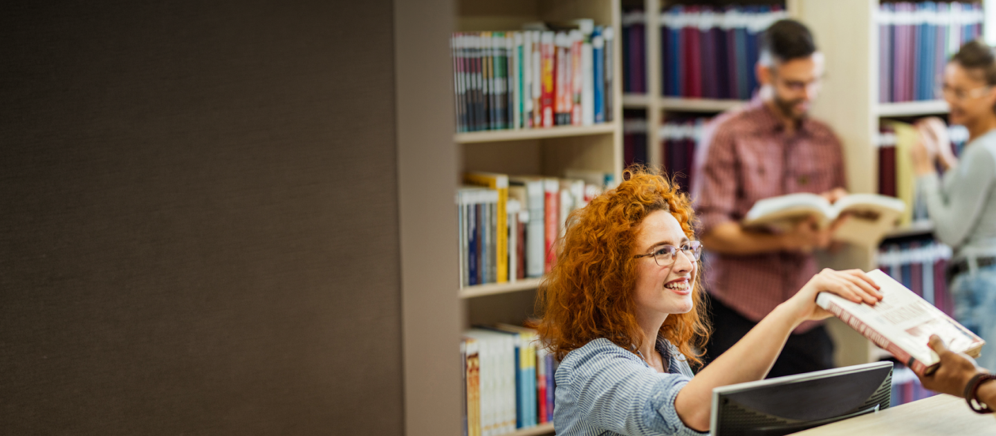 Librarian sat behind a desk, giving a book to someone