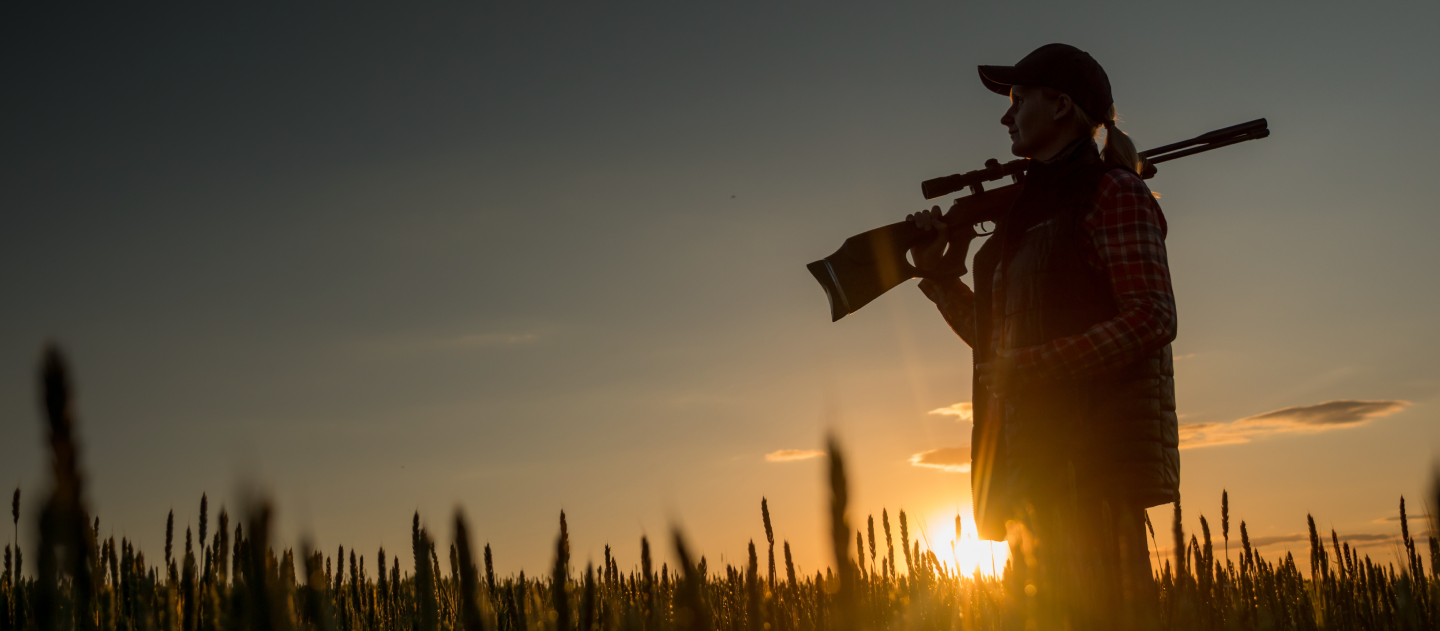Shadow of a woman holding her rifle in a field over sunset