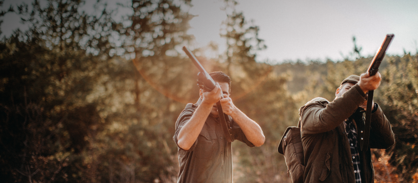 Two men aiming their shotguns in a forest