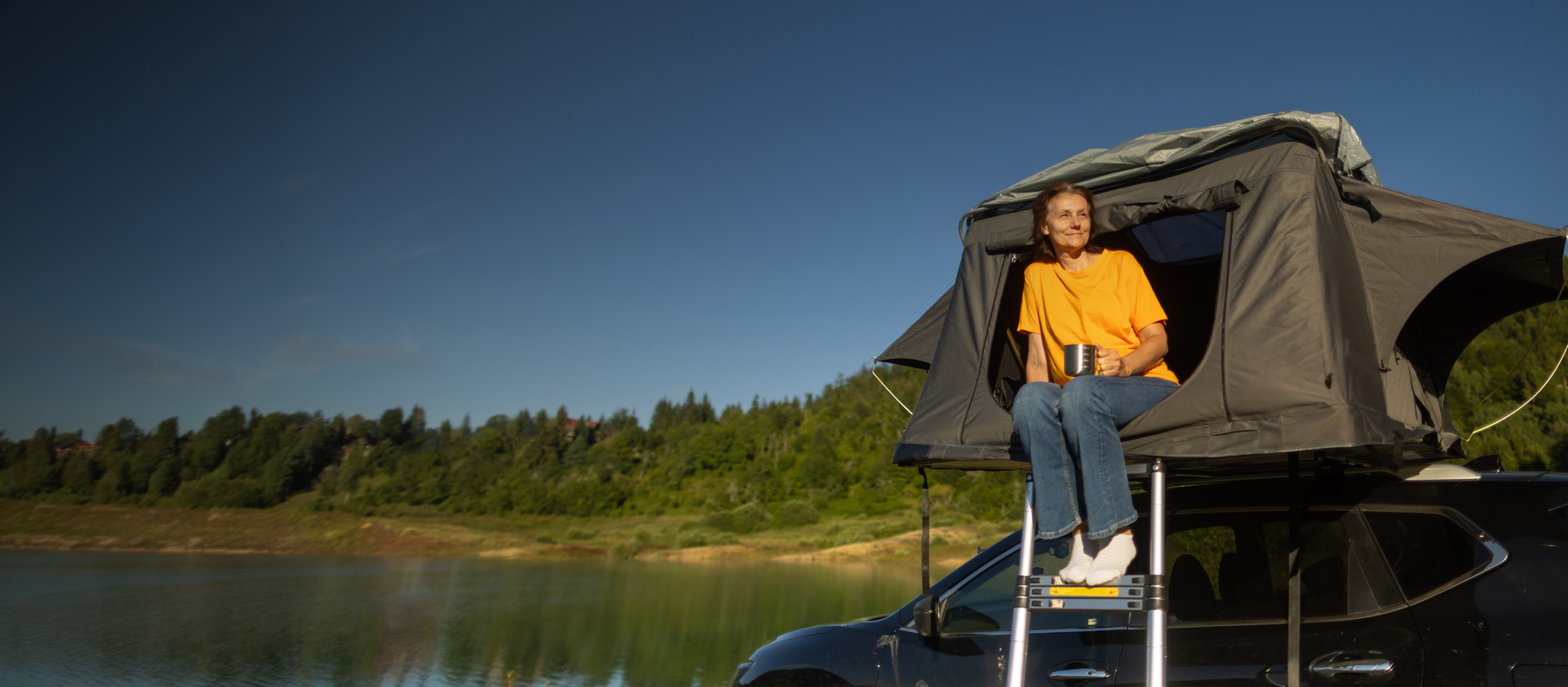 woman sat in her roof tent on top of a car