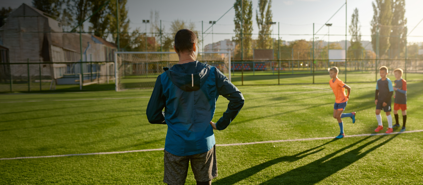 Man stood on a football pitch with children behind him